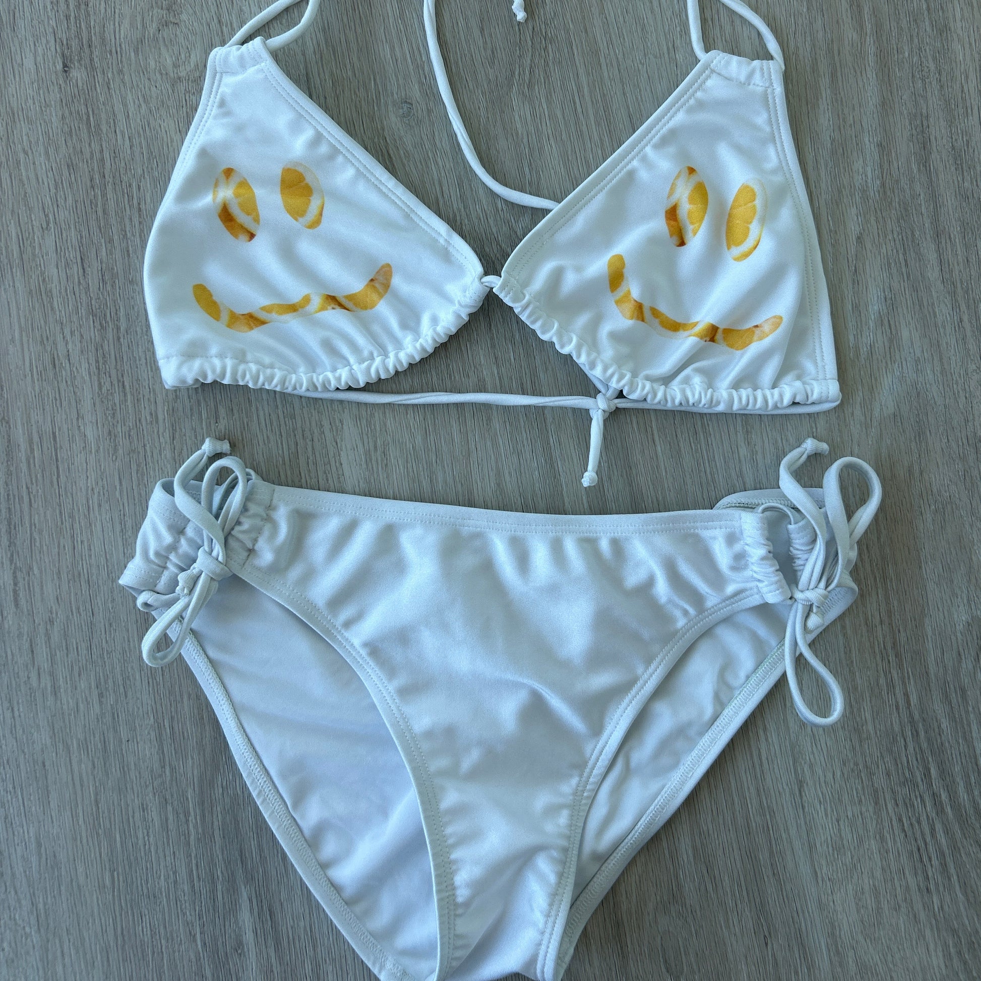 White bikini set with yellow floral patterns on a wooden surface