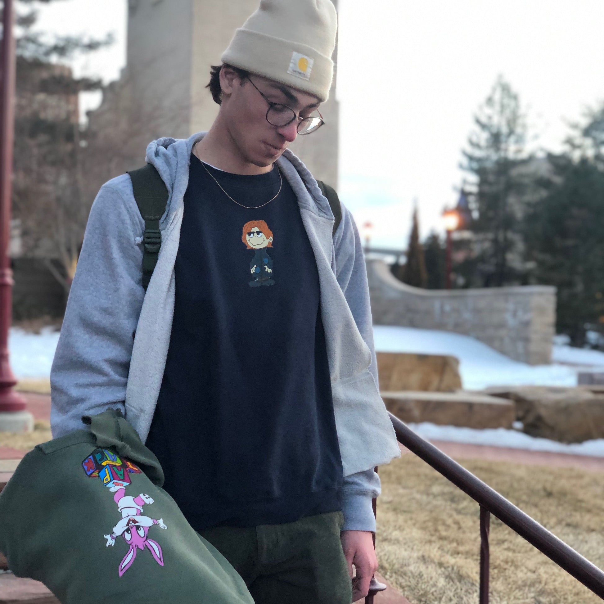 Person wearing a beanie and carrying a green jacket with colorful designs outdoors.