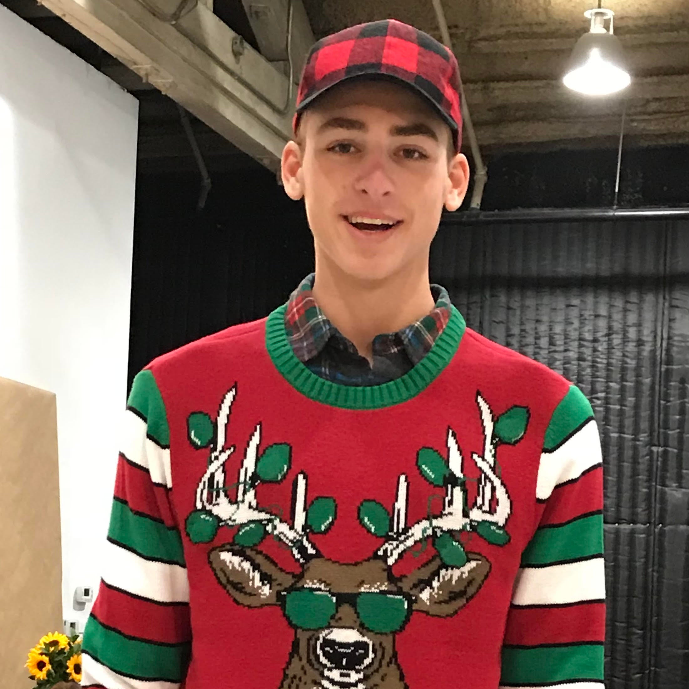 Person wearing a festive sweater with reindeer design and 'Let It Glow' text in an indoor setting.